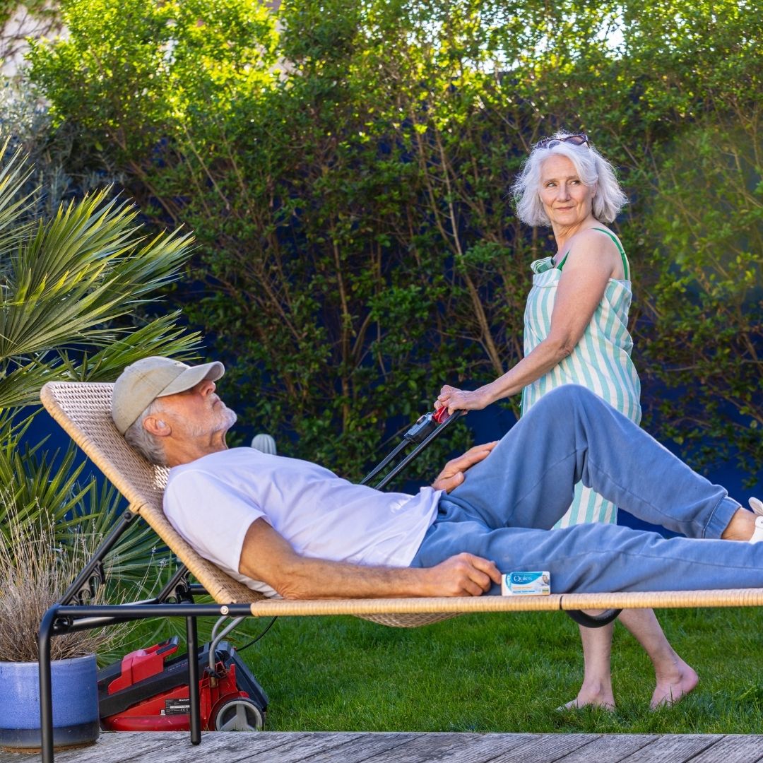 Homme se reposant dans un jardin avec des bouchons d'oreilles Quies Silicone pendant que sa femme tond la pelouse